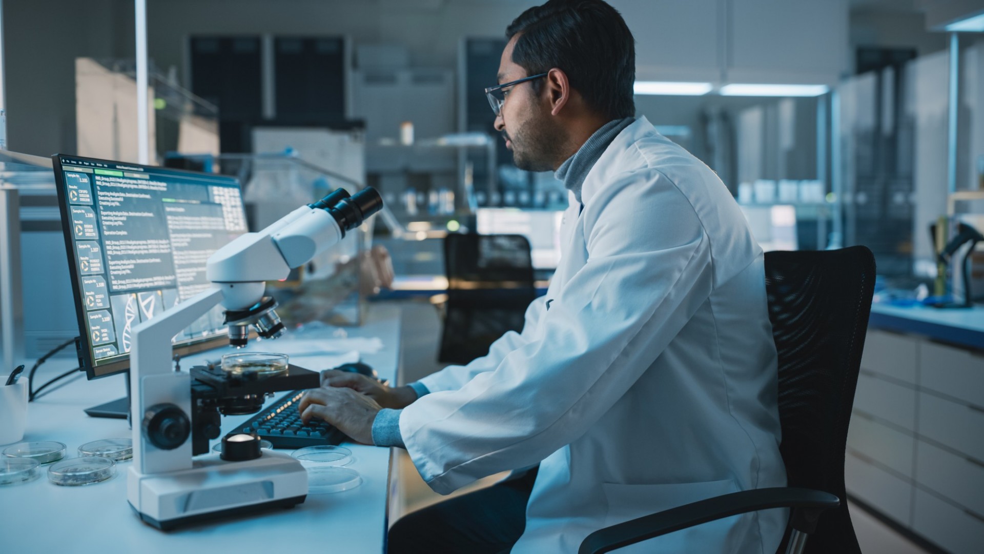 Taking Action: COVID-19 Diversity, Equity, & Inclusion Challenge Male scientist with glasses looking at computer screen with microscope in foreground