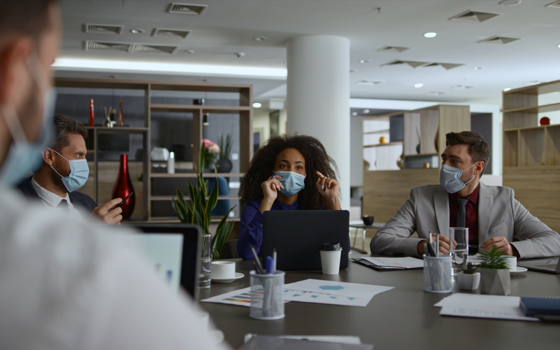 Businesspeople working at a conference table, wearing masks